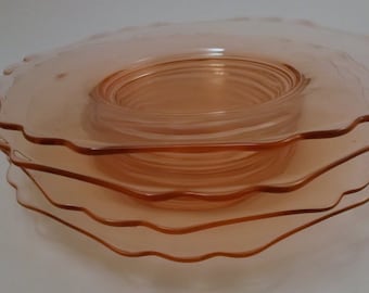 May include: A stack of four pink glass dessert plates with scalloped edges. The plates are stacked in a pyramid shape.