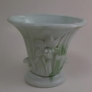 May include: A white ceramic vase with a green and white floral design. The vase is shaped like a bell and has a wide base.