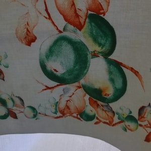 May include: A white linen tea towel with a green, orange, and white floral design. The design features apples and leaves.