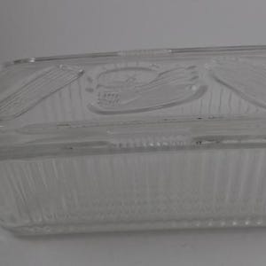 May include: A clear glass butter dish with a lid. The lid has a raised design of corn on the cob.