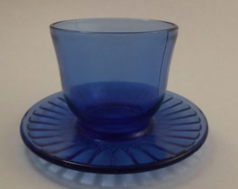 May include: A cobalt blue glass cup and saucer set. The saucer has a fluted design.