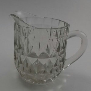 May include: A clear glass pitcher with a diamond pattern. The pitcher has a handle and a wide mouth.