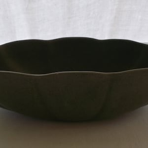 May include: A large, green ceramic bowl with a scalloped rim. The bowl is empty and has a smooth, matte finish.