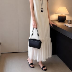 Peut inclure: Une robe longue sans manches de couleur crème avec une taille basse et un ourlet à volants, associée à un sac à main rectangulaire noir doté de fines bretelles, un collier pendentif noir et des sandales noires à bout ouvert.