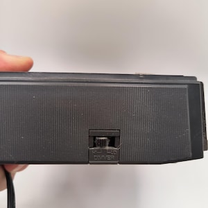 May include: A black electronic device with a textured surface and a dimmer switch labelled "HI-LO DIMMER". A black power cord extends from the device.