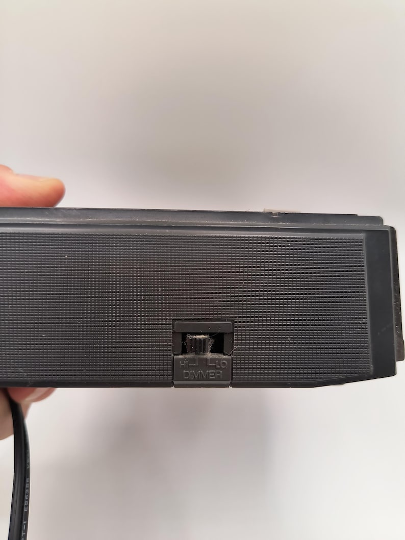 May include: A black electronic device with a textured surface and a dimmer switch labelled "HI-LO DIMMER". A black power cord extends from the device.