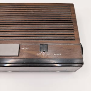 May include: A vintage brown wooden alarm clock with a slatted top. The clock has a silver snooze button and a power switch with settings for auto, off, and on. The word "POWER" is printed on the clock.