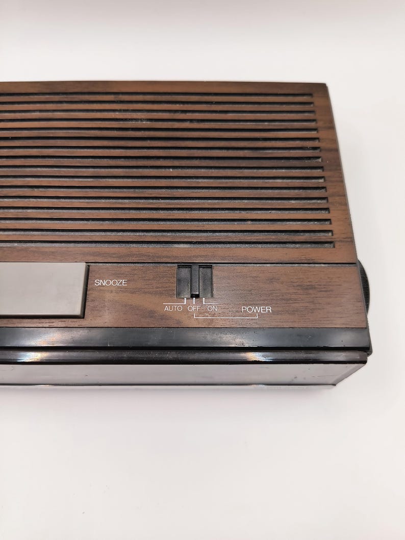 May include: A vintage brown wooden alarm clock with a slatted top. The clock has a silver snooze button and a power switch with settings for auto, off, and on. The word "POWER" is printed on the clock.