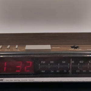 May include: A retro Emerson FM/AM digital clock radio with a brown wood-effect finish. The red digital display shows 1:32. Features include radio frequency dial, alarm, and battery backup.