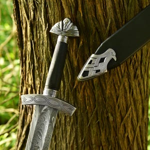 May include: A detailed image of a sword with a patterned blade and ornate silver hilt. The handle is black, and the scabbard is visible. The sword is leaning against a tree trunk, showcasing the craftsmanship.
