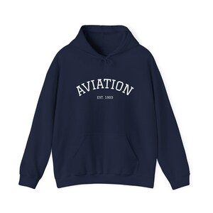 May include: Navy blue hoodie with a front pocket and drawstring hood. The word "AVIATION" is printed across the chest in white, with "EST. 1903" below it. A casual, comfortable garment.