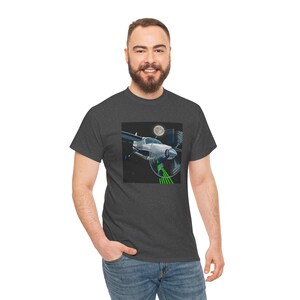 May include: Dark gray t-shirt featuring a graphic of a silver airplane with a spinning propeller, a full moon, and green lines. The t-shirt is made of a soft material and has a crew neck.