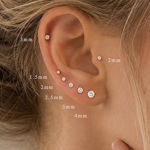 May include: A set of seven small round stud earrings with clear stones, arranged along the earlobe and cartilage. The sizes are labelled as 1.5 mm, 2 mm, 2.5 mm, 3 mm, and 4 mm, indicating the diameter of each individual stud earring in the set.
