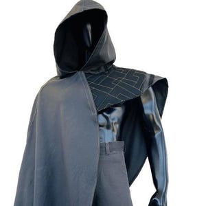 May include: A dark gray hooded cloak and matching pants set displayed on a mannequin. The cloak features a cape-like design with a geometric pattern on the shoulders. The pants have a tailored fit. The outfit is suitable for cosplay or costume events.