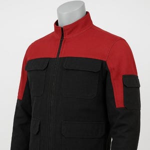 Pode incluir: Casaco preto com gola e detalhes vermelhos nos ombros. O casaco tem zíper total, gola alta e quatro bolsos frontais. As mangas são compridas e o casaco parece ser feito de um tecido durável.