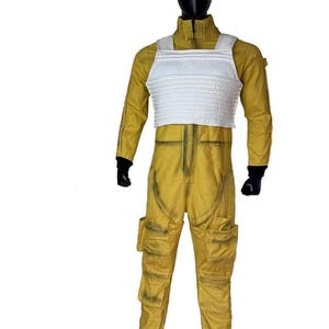 May include: A yellow jumpsuit with a white chest plate, displayed on a mannequin. The jumpsuit has multiple pockets and black gloves. The outfit is designed with a weathered appearance.