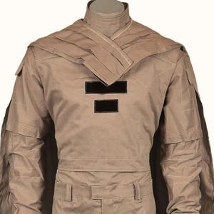 May include: Tan-colored military-style uniform with a high collar and a layered shoulder design. The uniform features two black rectangular patches on the chest and multiple pockets. The fabric appears to be a durable, possibly water-resistant material.