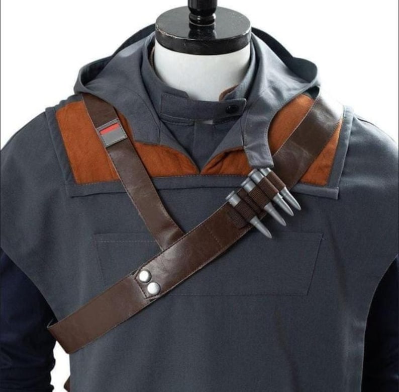 May include: A gray hooded jacket with brown leather shoulder straps and accents. The jacket features a brown leather strap with silver studs and a small red and gray patch. The jacket is part of a costume.