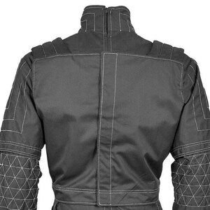 May include: A dark gray racing suit with white stitching. The suit features a high collar, padded shoulders, and geometric patterns on the sleeves. The back of the suit is visible, showcasing the vertical and horizontal seams.