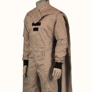 May include: A tan-colored costume with a high collar and cape. The outfit features black accents on the chest and black cuffs. The costume includes a long-sleeved jacket and matching pants. The mannequin is wearing black gloves.