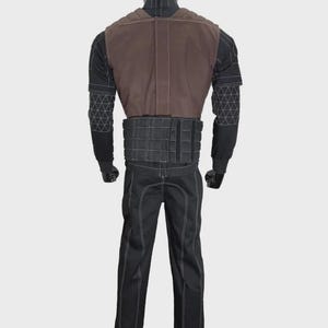 K&ouml;nnte beinhalten: Ein Kost&uuml;m bestehend aus einer braunen Weste, einem schwarzen Oberteil mit geometrischen Mustern, einem schwarzen G&uuml;rtel und einer schwarzen Hose mit wei&szlig;en N&auml;hten. Das Kost&uuml;m wird auf einer Schaufensterpuppe pr&auml;sentiert.