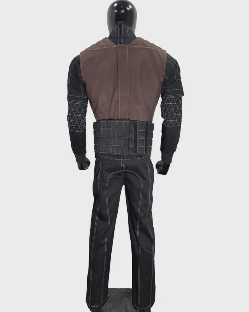 K&ouml;nnte beinhalten: Ein Kost&uuml;m bestehend aus einer braunen Weste, einem schwarzen Oberteil mit geometrischen Mustern, einem schwarzen G&uuml;rtel und einer schwarzen Hose mit wei&szlig;en N&auml;hten. Das Kost&uuml;m wird auf einer Schaufensterpuppe pr&auml;sentiert.