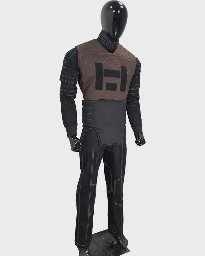 K&ouml;nnte beinhalten: Eine Schaufensterpuppe in einem taktischen Outfit in Schwarz und Braun. Das Outfit umfasst eine braune Weste mit einem gro&szlig;en schwarzen "H"-Logo, eine schwarze Hose mit wei&szlig;en N&auml;hten und ein schwarzes Langarmshirt. Die Schaufensterpuppe hat einen schwarzen Kopf und Handschuhe.