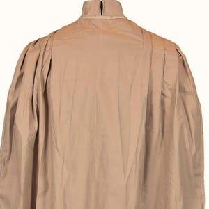 May include: A tan-colored cape with a high collar and a pleated design on the shoulders. The cape is made of a lightweight fabric and has a flowing silhouette. The back view of the cape is shown against a white background.