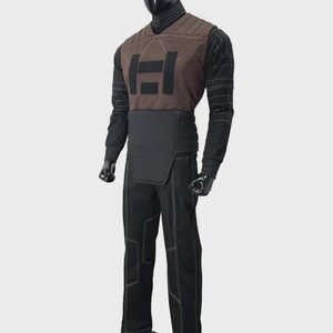 K&ouml;nnte beinhalten: Ein Ganzk&ouml;rperkost&uuml;m, das auf einer Schaufensterpuppe pr&auml;sentiert wird. Das Kost&uuml;m umfasst eine braune Weste mit schwarzem Logo, ein schwarzes Langarmshirt, eine schwarze Hose mit wei&szlig;en N&auml;hten und einen schwarzen G&uuml;rtel. Die Schaufensterpuppe ist schwarz.