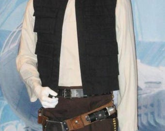 May include: A costume display featuring a black vest with four pockets, a cream-colored shirt, and brown pants. The outfit includes a utility belt with a holster and a blaster. The mannequin is on display.