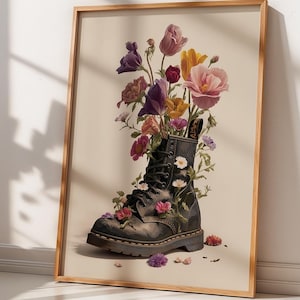 Puede incluir: Impresión artística enmarcada que muestra una bota militar negra llena de flores vibrantes. Las flores son una mezcla de rosas, moradas y amarillas. La bota, con sus cordones y costuras, se encuentra sobre un fondo neutro, en un marco de madera.