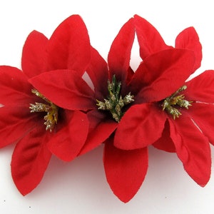 May include: Two red poinsettia flowers with glitter accents. The flowers are made of fabric and are perfect for holiday decorating.