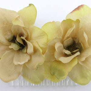 May include: A pair of beige fabric flower hair clips with a comb attachment. The flowers are made of a soft, delicate fabric and have a slightly ruffled appearance.