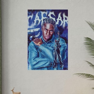 Puede incluir: Un póster de retrato con un hombre con una chaqueta vaquera, sosteniendo una estatua. El fondo tiene texto estilo grafiti que dice "CAESAR" en blanco y azul. El hombre lleva una pulsera dorada.