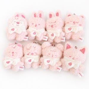 Puede incluir: Ocho llaveros de peluche rosa con forma de animales, como osos, conejos y gatos. Cada uno tiene un lazo blanco, un corazón y los ojos cerrados. Los llaveros tienen una pequeña etiqueta que dice "2020".