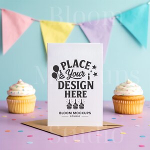 May include: A white greeting card with the text "Place Your Design Here" is propped up on a brown envelope. Two cupcakes with white frosting and sprinkles sit on either side. A colorful banner hangs in the background.