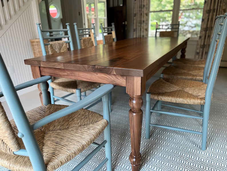 May include: A large, rectangular, wooden dining table with a dark brown walnut finish. The table has turned legs and is surrounded by six blue chairs with woven cane seats.