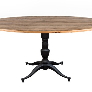 May include: Round wooden table with a black pedestal base and four legs. The table top is made of reclaimed wood with a natural finish.