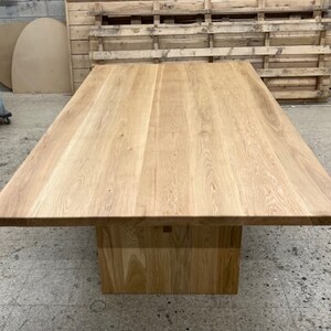 May include: A large, rectangular, wooden dining table with a natural wood finish. The table has a thick, solid top and a simple, square base.