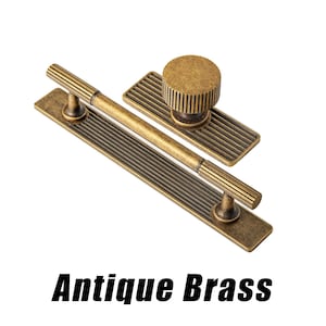 Puede incluir: Juego de herrajes para armarios de lat&oacute;n antiguo. El juego incluye un tirador largo con dos postes, un pomo con base rectangular y un tirador m&aacute;s peque&ntilde;o. El herraje tiene un dise&ntilde;o acanalado y un acabado vintage. El texto "Antique Brass" est&aacute; en la parte inferior.