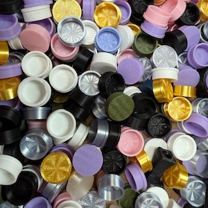 May include: A collection of colorful, assorted cosmetic containers and lids. The lids and containers are in various colors, including pink, purple, gold, black, and silver. The containers have a variety of textures and designs.