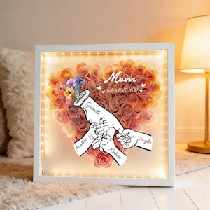 May include: A white framed artwork featuring a heart made of peach-coloured roses. The words "Mom, we love you" are above a drawing of hands holding each other. The names "Giselle", "Hattie", "Kohen", and "Jayla" are also visible.