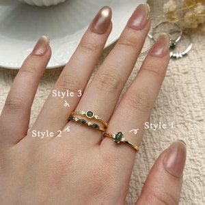 May include: Three gold rings with green gemstones and small diamonds are displayed on a hand. The rings are labelled "Style 1", "Style 2", and "Style 3". The rings are on a beige surface. The text "Dear Letter" is at the bottom.