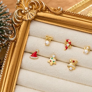 Könnte beinhalten: Ein Set aus sechs goldfarbenen Ohrsteckern mit weihnachtlichen Motiven, darunter eine Schleife mit Perle, eine Zuckerstange, ein Schneemann mit Perle, eine rote Weihnachtsmütze, ein Weihnachtsbaum mit bunten Akzenten und eine Glocke mit Stein.