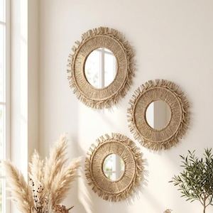 Puede incluir: Tres espejos de pared redondos con marcos de cuerda natural y bordes con flecos. Los espejos son de diferentes tamaños y están montados en una pared de color claro. Los espejos tienen un estilo bohemio o costero.