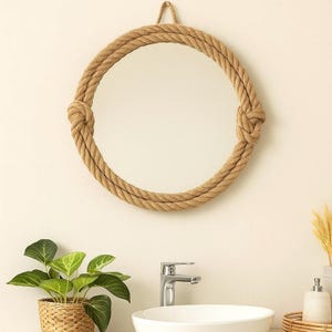 Peut inclure: Un miroir rond avec un cadre en corde naturelle épaisse. La corde est nouée en deux points, ajoutant une touche nautique. Le miroir est accroché à un mur de couleur claire, créant un design simple mais élégant.