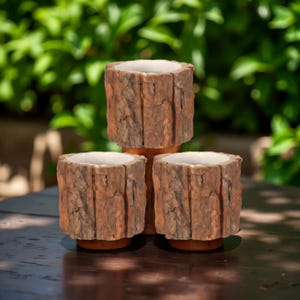 Peut inclure: Trois jardinières décoratives avec un design rustique en forme de bois. Les jardinières ont une forme cylindrique avec un extérieur brun texturé ressemblant à de l'écorce d'arbre. L'intérieur de chaque jardinière est blanc. Les jardinières sont disposées sur une surface en bois.