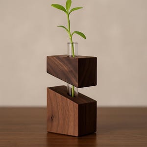 May include: A contemporary wooden vase featuring two angled, dark brown blocks. Clear glass tubes hold a green plant with small leaves. The vase is a decorative item for displaying small plants or flowers.
