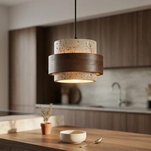 Peut inclure: Un luminaire suspendu moderne avec un design en couches. La partie supérieure est beige moucheté, suivie d'une bande en bois foncé et d'une partie inférieure beige. La lumière est suspendue à un cordon noir, éclairant une cuisine.
