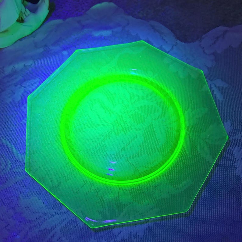 May include: A glowing green octagonal plate with a floral pattern. The plate has a circular center and a raised rim. The plate is made of glass and glows brightly under a black light.